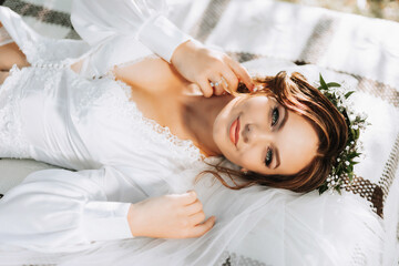 portrait of a dreamy bride lying on a bed in a garden under a tree. The bride is wearing a white...