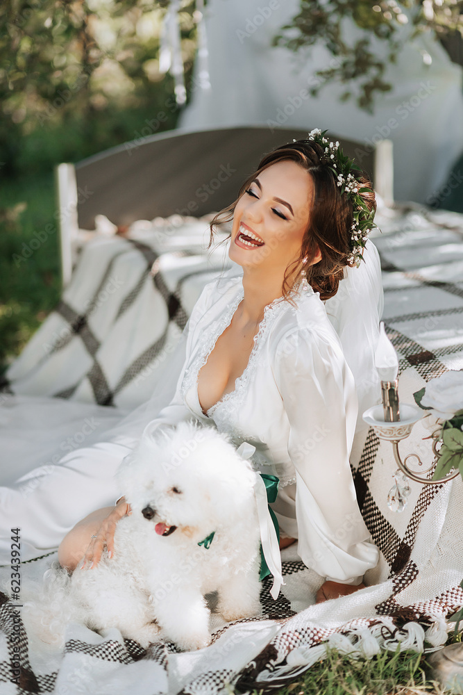 Wall mural young elegant bride in a white dress with a tiara of fresh flowers on her head posing in the garden 