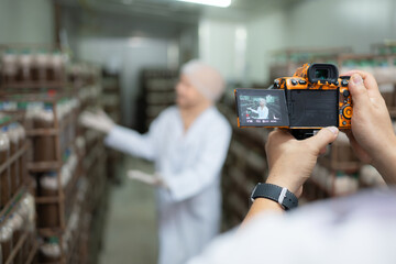 A photographer holding a digital camera on a production line is recording the work of a mushroom house worker. To be used for public relations and further marketing