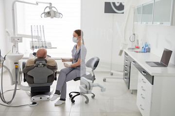 Portrait of young female dentist standing by mid adult man in clinic. Female dentist repairing...