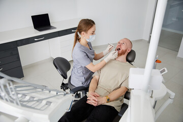 Portrait of young female dentist standing by mid adult man in clinic. Female dentist repairing...