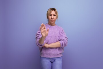 portrait of a shocked surprised blond young woman in a casual look shows her hand to the side on a bright background with copy space