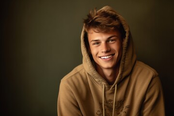 Lifestyle portrait photography of a grinning boy in his 20s wearing a comfortable hoodie against a warm taupe background. With generative AI technology
