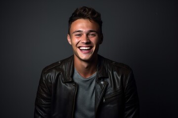 Medium shot portrait photography of a grinning boy in his 30s wearing a trendy leather jacket against a cool gray background. With generative AI technology