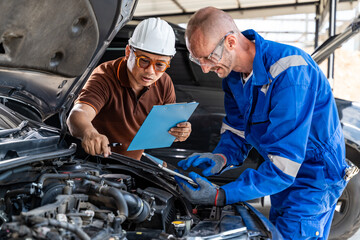 Two male car mechanics working together on the car engine at their car repair garage