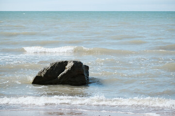 Rocks in the sea. Sea waves on a sandy beach.