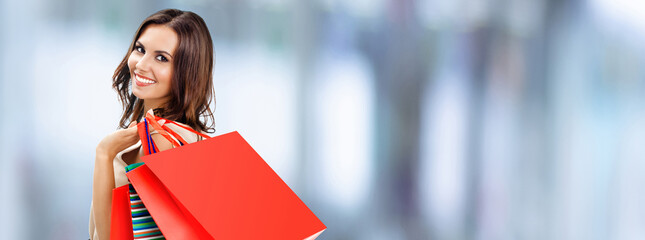 Image of shopping woman. Happy smiling girl holding grocery bags, on blurred modern mall background. Copy space for some text. Brunette model - consumerism, sales and shopaholic concept picture.