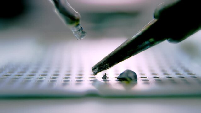 Silver melted metal drops falling down on devi8ce panel under light. Soldering device melts metal on special stick closeup