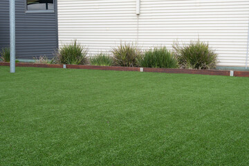 Background texture of green artificial turf with timber garden edge against a weatherboard...