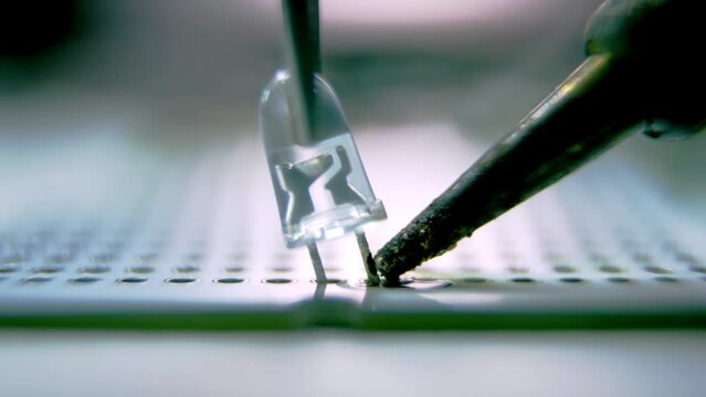 Soldering of small led bulb on device panel with help of pincers. Installation of led light with soldering device and pincers closeup