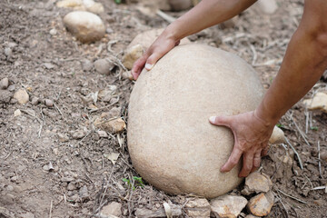 Close up hand is lifting big stone from ground. Concept, heavy. Hard working. Strong body to lift or move heavy rock. 