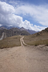 The cloudy blue sky overlooking dusty path towards the mountains 

The cloudy blue sky provides a breathtaking backdrop as it stretches endlessly above. 