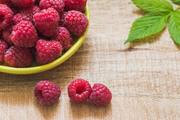 Fresh raspberries in a small yellow bowl on a cutting board. Fruits on a wooden background. © Taste the Image