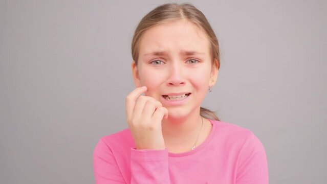 A little girl in a pink t-shirt is crying and screaming. Video in the studio on a gray background. Close-up portrait of a girl.