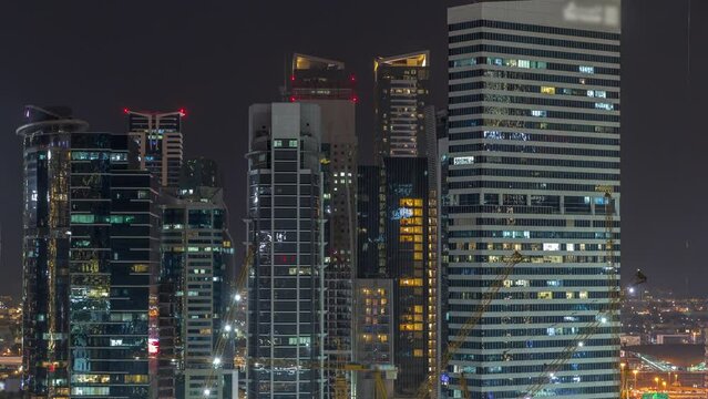 Cityscape with illuminated skyscrapers of Dubai Business Bay and water canal aerial night timelapse. Modern skyline with residential and office towers on waterfront. Construction cranes in front