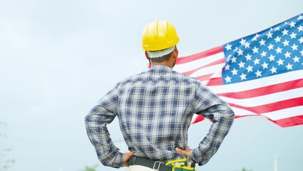 Confidently standing construction working with safety hat in front of waving American Flag - concept of Independence day or Labours day celebration
