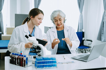 Two scientist or medical technician working, having a medical discuss meeting with an Asian senior female scientist supervisor in the laboratory with online reading, test samples and innovation 
