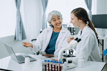 Two scientist or medical technician working, having a medical discuss meeting with an Asian senior female scientist supervisor in the laboratory with online reading, test samples and innovation 