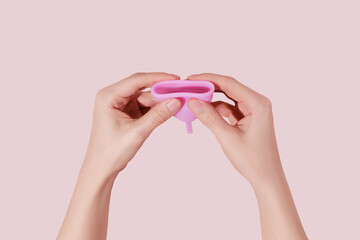 Female hand with reusable menstrual cup on pink background