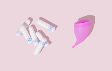 Pink reusable silicone menstrual cup and tampons on pink background. Top view. Concept of feminine...