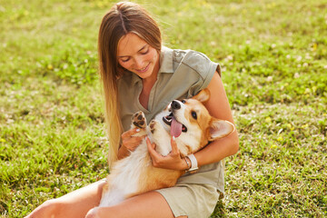 a young girl holds a cheerful and funny Welsh Corgi in her arms in a park in sunny weather, the concept of happy dogs