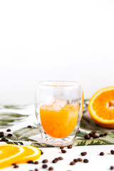 Full glass of orange juice close-up. Fresh orange juice with ice and coffee beans on the table. Sliced orange on the background