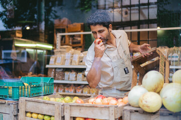 Latin man greengrocer smelling an organic red apple in his organic vegetable shop