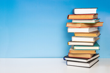 Stack of books in the colored cover lay on the wooden  table and blue backround. Education learning...