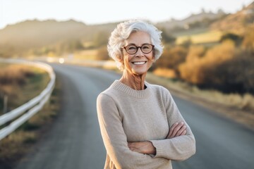 Fototapeta na wymiar Lifestyle portrait photography of a satisfied old woman wearing an elegant long-sleeve shirt against a winding country road background. With generative AI technology