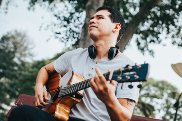 Portrait of young man playing acoustic guitar sitting in a park. Concept of people and hobbies.