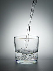 Pouring water into a glass on gray background. Shallow depth of field