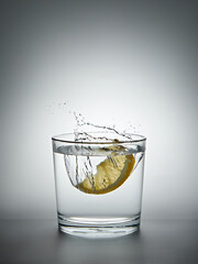 lemon splashing into a glass of water on a gray background