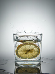lemon splashing into a glass of water on a gray background