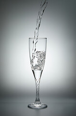 Pouring water into a glass on gray background. Shallow depth of field.