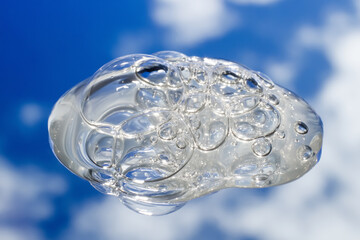Spilled transparent bubbly gel in close-up. Against a backdrop of mirrored clouds and sky