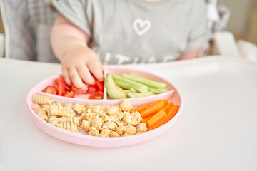 Cute child eats healthy food pasta and vegetables steamed,. Portraits of a cute 10 months old baby girl. The baby sitting in a special high chair for babies. 
