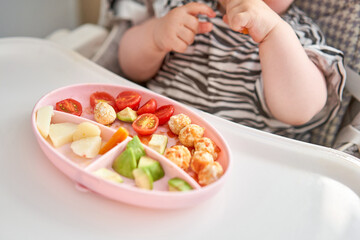 Cute child eats healthy food vegetables and meatballs from dietary meat steamed,. Portraits of a cute 10 months old baby girl. The baby sitting in a special high chair for babies.