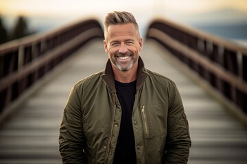 Eclectic portrait photography of a grinning mature man wearing a sleek bomber jacket against a rustic bridge background. With generative AI technology