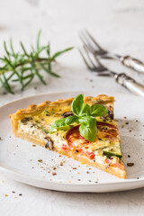 Piece of vegetable tart with mushrooms, tomatoes and zucchini on white background, vertical