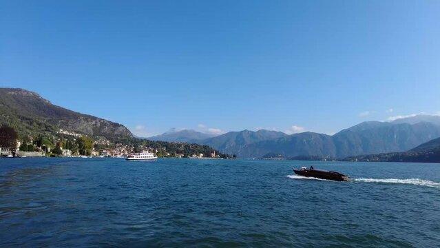 Lake Como from Lenno Port, see ferry boat and taxi boat cruising on beautiful blue lake.
