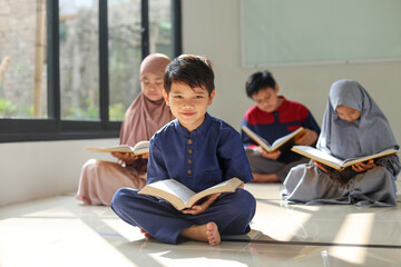 A cute little boy smiling at camera after reading the Koran or Quran. Selective focus with his...