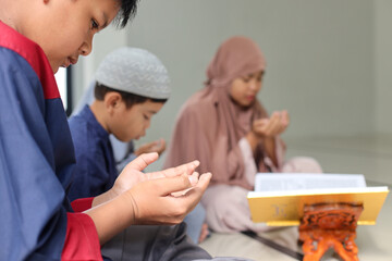 Asian muslim teen boy praying dua after or before reading Quran together with multiethnic friends...
