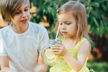 Children drink natural lemonade at stand in park. Summer refreshing natural drink lemonade. Detox fruit infused flavored water, cocktail in a beverage dispenser with fresh fruits - obrazy, fototapety, plakaty