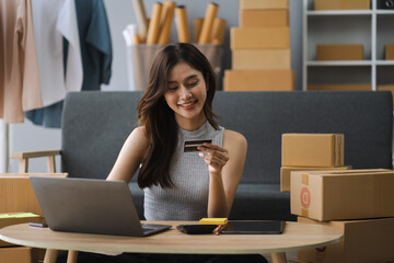 Asian woman holding credit card and using laptop. woman working at home. Online shopping, e-commerce, internet banking, spending money, working from home concept.