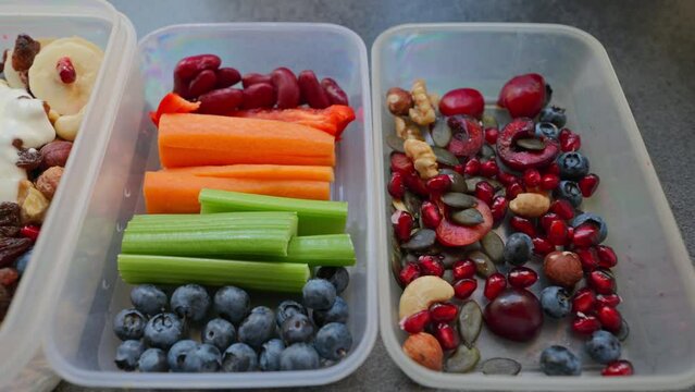 Boxes with healthy food full of colorful vegetables and fruits. Nuts, blueberries, yogurt, pomegranates, bananas, gluten-free pancakes, raisins, celery, carrots and peppers. Meals for the day. 