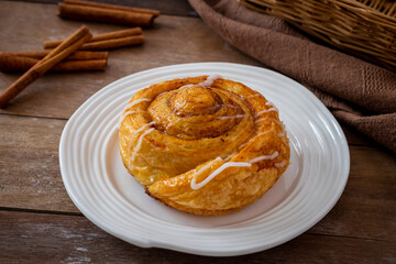 Cinnamon roll bun on white plate and cinnamon sticks on wooden table
