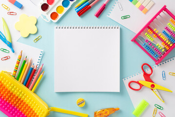 Embark on a learning adventure with this creative top view composition: colorful collection of childish school supplies on serene pastel blue surface, with blank notebook page for text or advertising