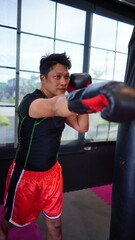 Thai boxing man in gym with sandbag. Athlete man in fitness with glove train in punching and kicking. Martial art exercise for strength.