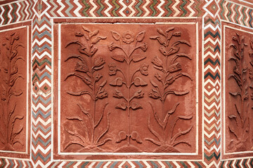 Decorative flowers on red sandstone wall of Taj Mahal, beautiful ancient wall decorations depicting flowers plants, old red sand stone handmade ornament decoration in Taj Mahal landmark building