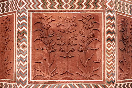 Decorative flowers on red sandstone wall of Taj Mahal, beautiful ancient wall decorations depicting flowers plants, old red sand stone handmade ornament decoration in Taj Mahal landmark building